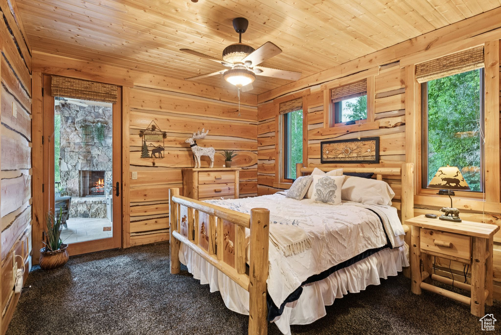 Bedroom with wooden ceiling, dark colored carpet, access to outside, wooden walls, and a fireplace