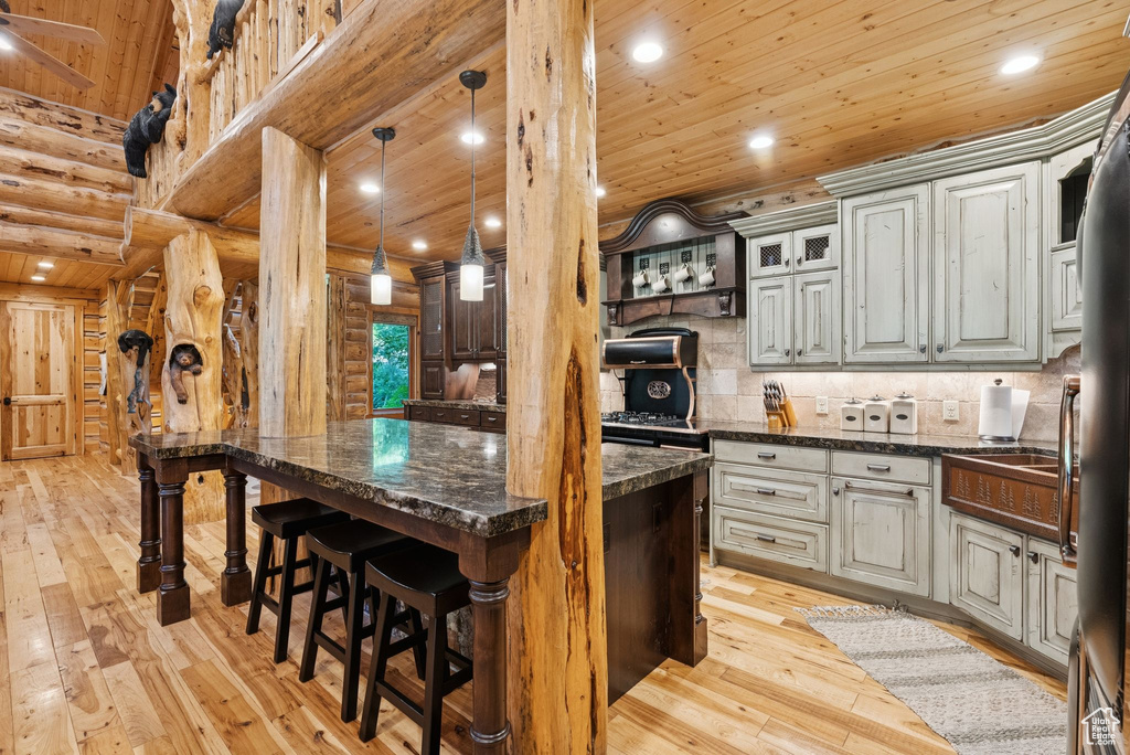 Kitchen with log walls, wooden ceiling, light wood-style floors, a breakfast bar area, and a kitchen island