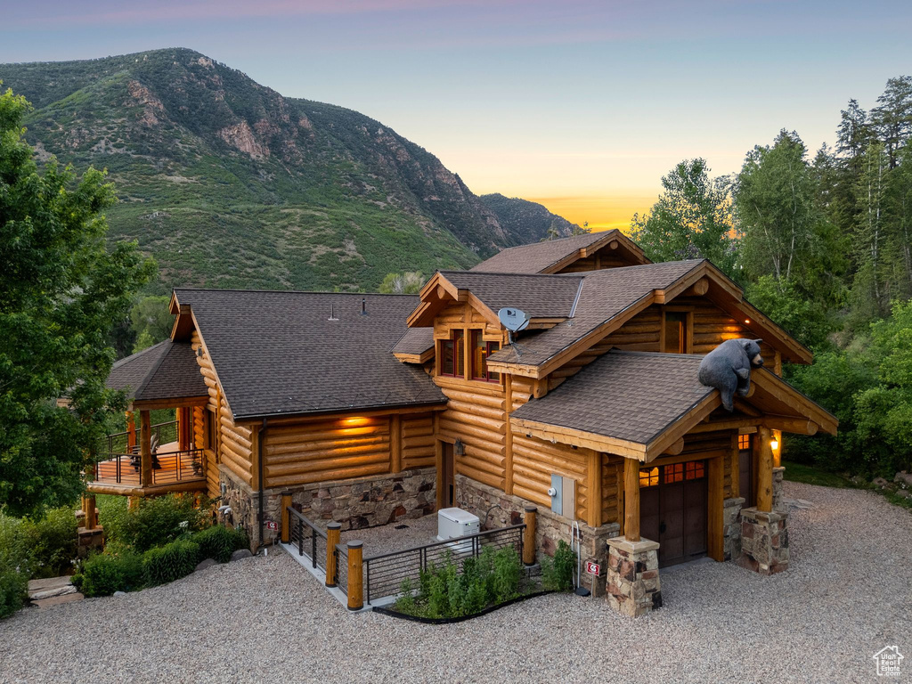 Log cabin with driveway, stone siding, a garage, a shingled roof, and a mountain view