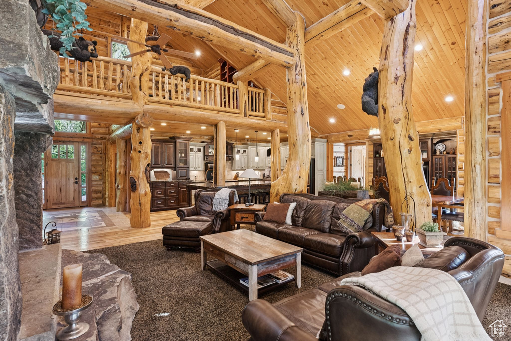 Living room with high vaulted ceiling, a wooden ceiling with exposed beams, log walls, ceiling fan, and recessed lighting