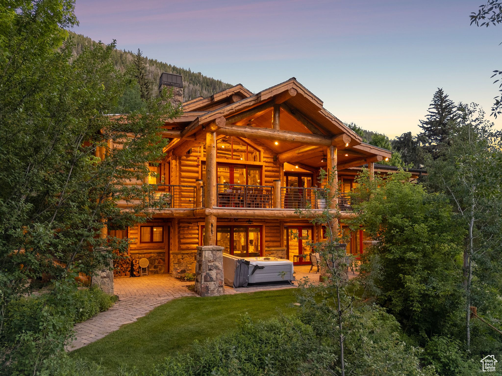 Back of house featuring a hot tub, a balcony, log siding, a patio area, and a chimney