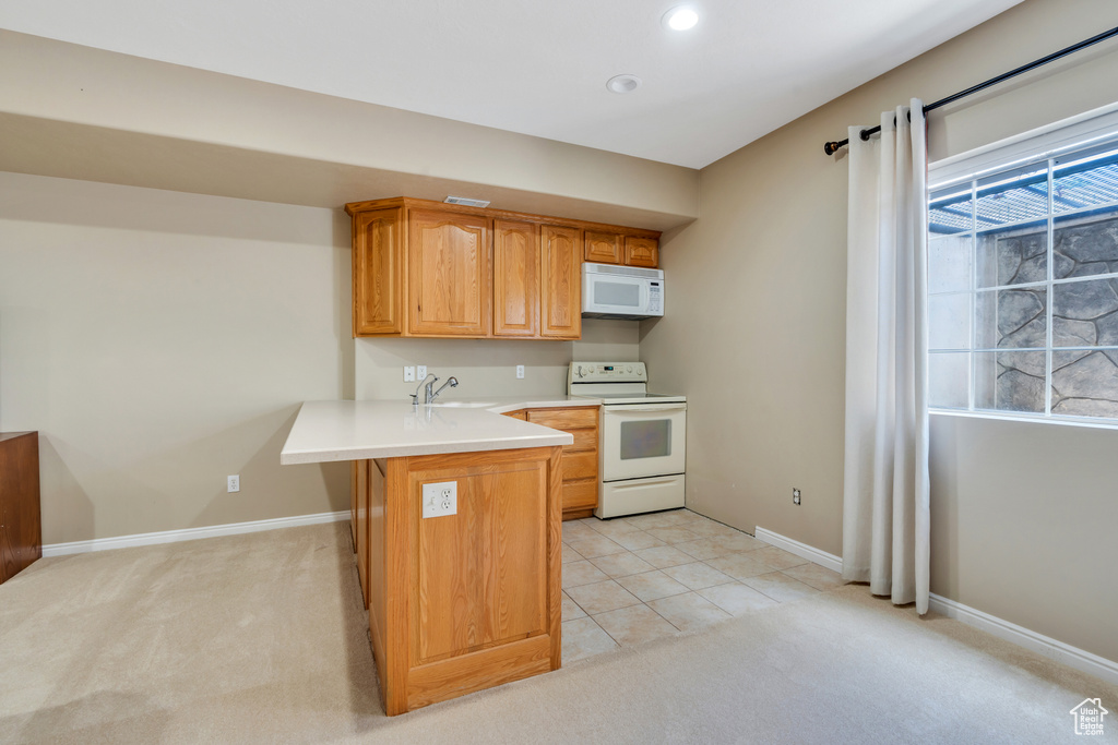 Kitchen featuring white appliances, a peninsula, light countertops, recessed lighting, and light colored carpet