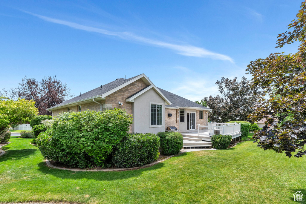 View of front of house featuring a front lawn, a wooden deck, brick siding, and roof with shingles