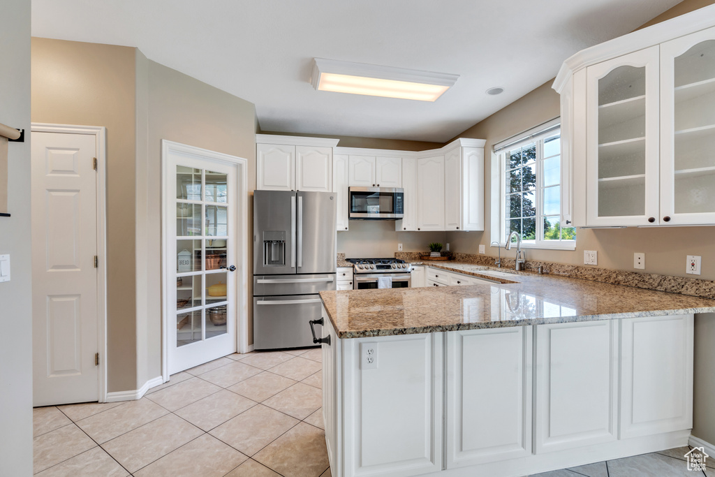 Kitchen featuring stainless steel appliances, a peninsula, light stone counters, glass insert cabinets, and white cabinets