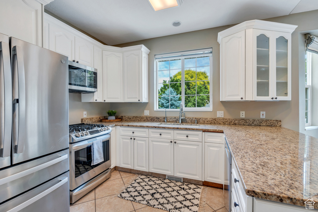 Kitchen with appliances with stainless steel finishes, white cabinets, glass insert cabinets, light stone countertops, and light tile patterned flooring
