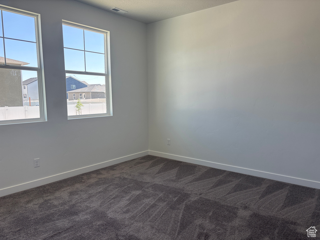 Unfurnished room featuring plenty of natural light and dark colored carpet