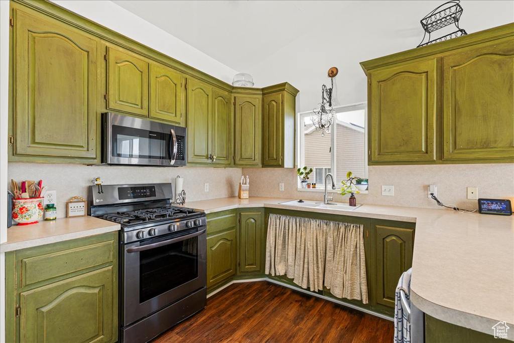 Kitchen featuring appliances with stainless steel finishes, light countertops, dark wood-style flooring, decorative light fixtures, and tasteful backsplash
