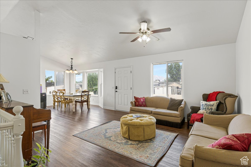 Living room with lofted ceiling, plenty of natural light, a chandelier, ceiling fan, and dark wood-style flooring