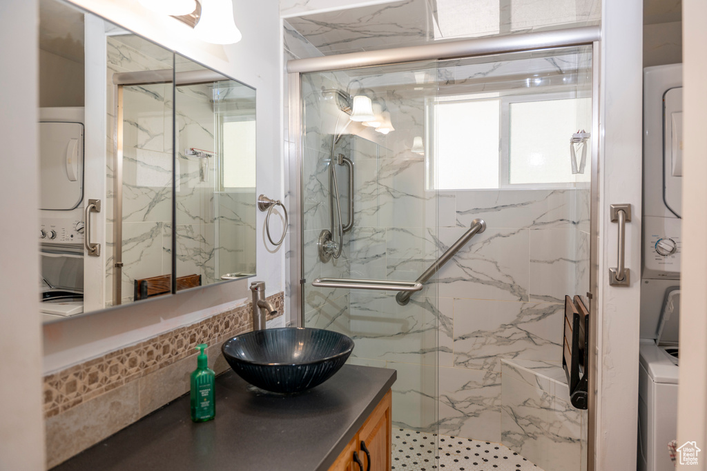 Bathroom with stacked washing machine and dryer, a marble finish shower, and vanity
