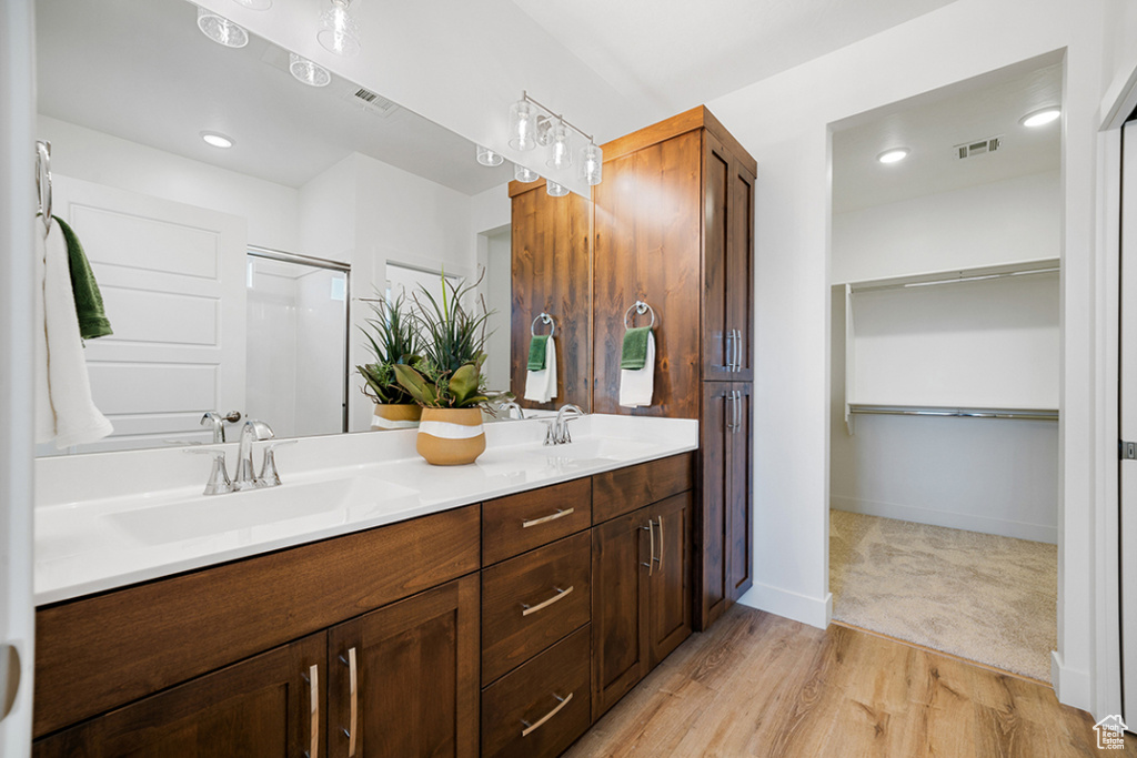 Bathroom with double vanity, wood finished floors, a spacious closet, and a shower with door