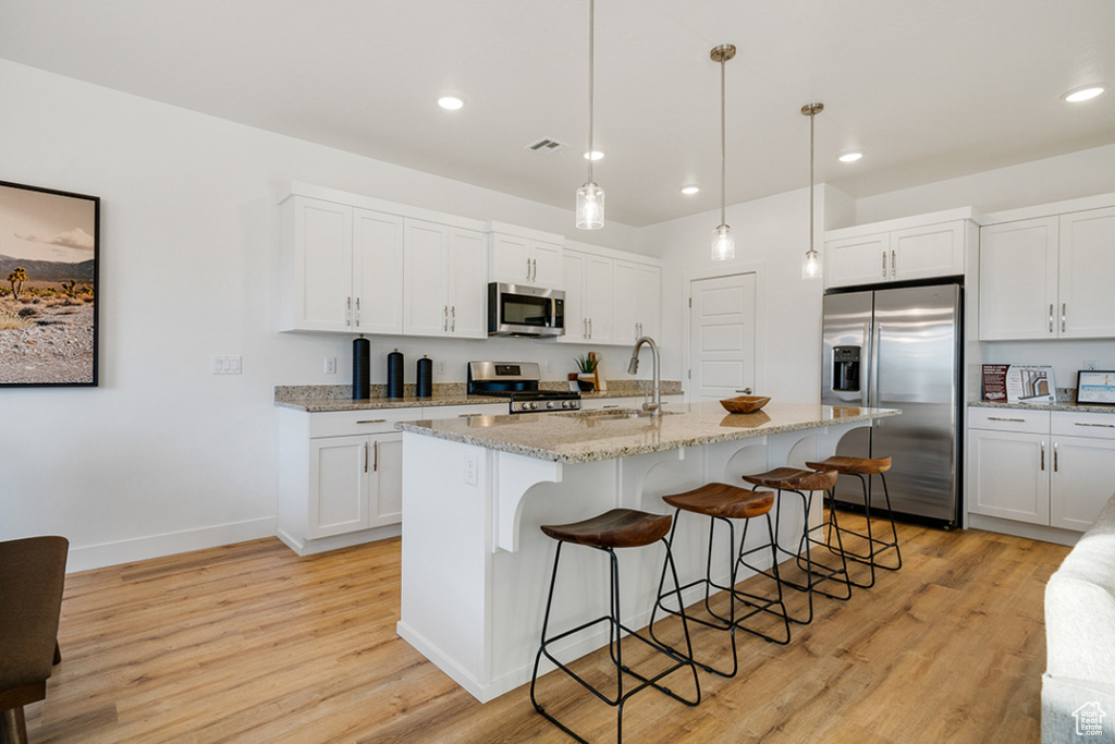 Kitchen with appliances with stainless steel finishes, light wood finished floors, a breakfast bar, white cabinetry, and recessed lighting