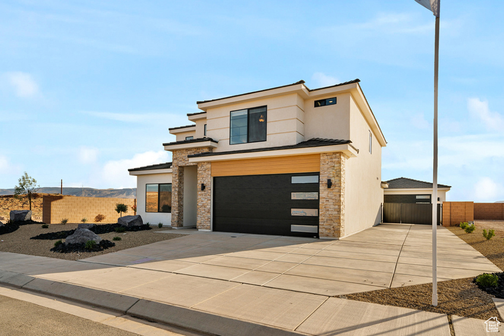Modern home featuring an attached garage, driveway, stone siding, and stucco siding