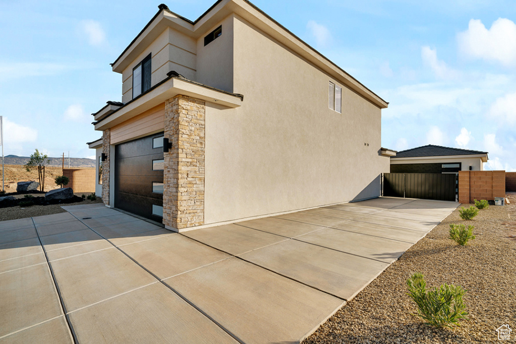 View of property exterior with stone siding, an attached garage, concrete driveway, and stucco siding