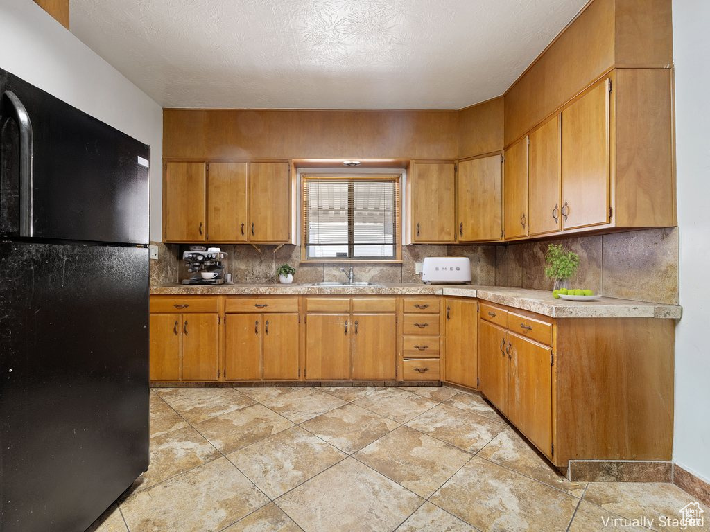 Kitchen with freestanding refrigerator, light countertops, decorative backsplash, and brown cabinetry