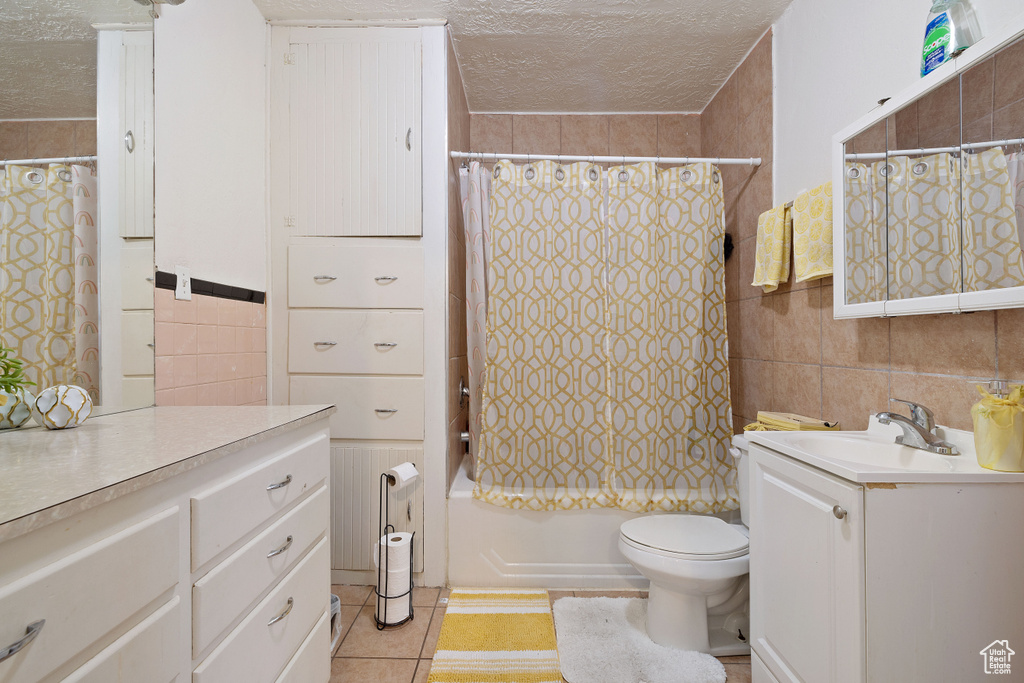 Full bathroom featuring tile walls, a textured ceiling, vanity, shower / bath combo with shower curtain, and tile patterned flooring