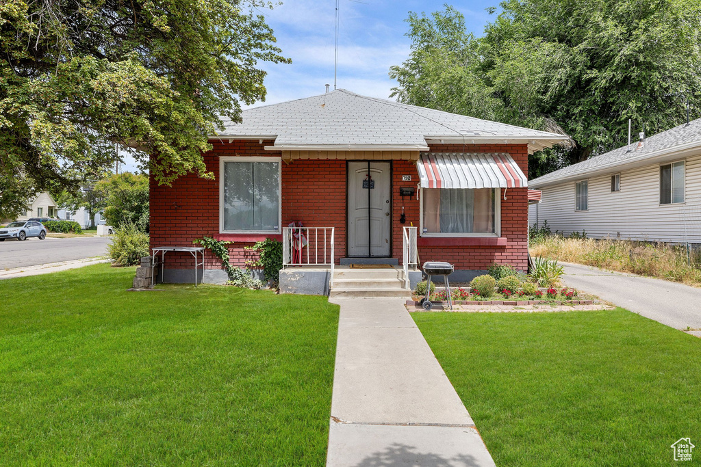 Bungalow-style home with brick siding, a front yard, and a shingled roof