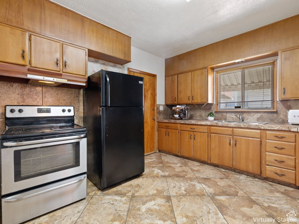 Kitchen with electric stove, freestanding refrigerator, under cabinet range hood, decorative backsplash, and light countertops