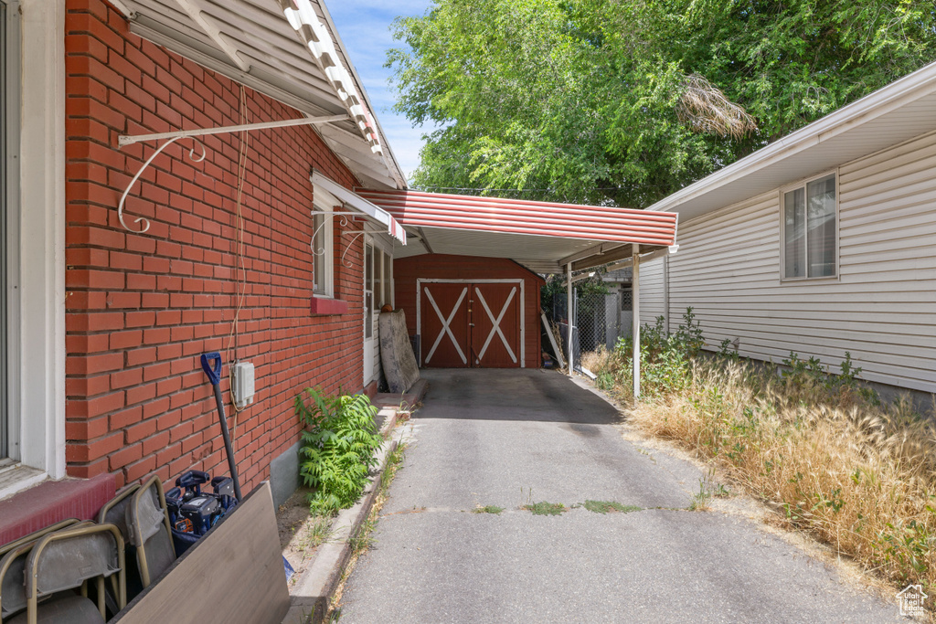 View of car parking with a storage unit, asphalt driveway, and an attached carport