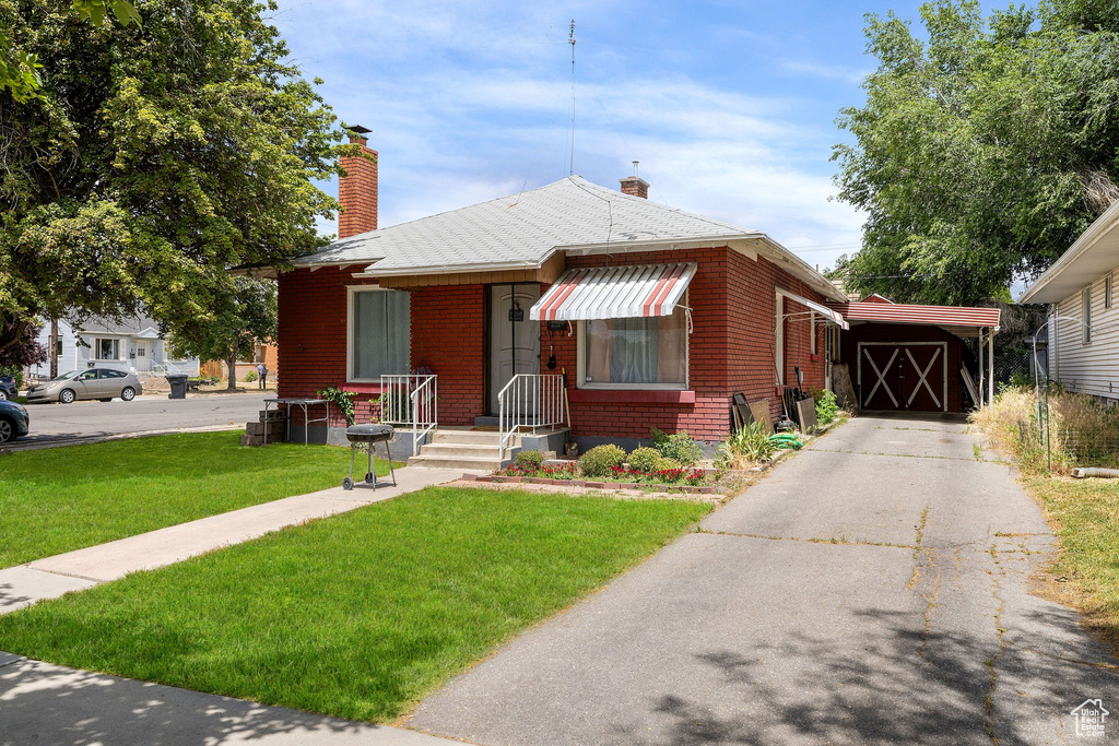 Bungalow-style home with a front yard, a chimney, brick siding, and driveway
