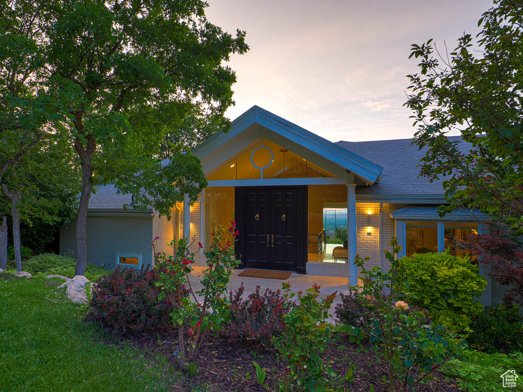 View of front facade with covered porch, a shingled roof, and brick siding
