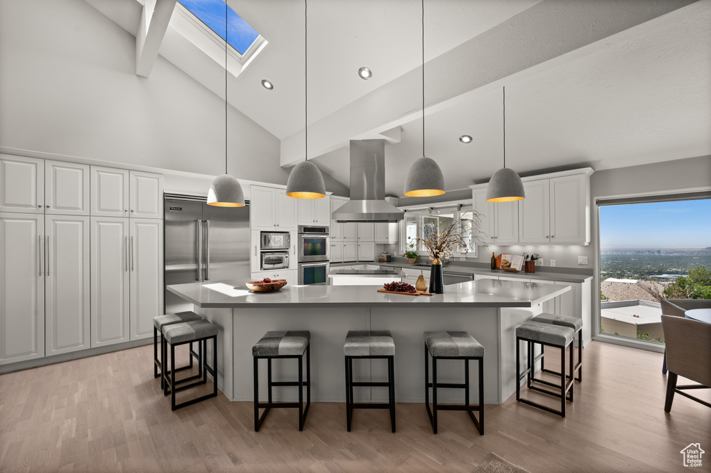 Kitchen featuring island range hood, a skylight, high vaulted ceiling, built in appliances, and white cabinetry