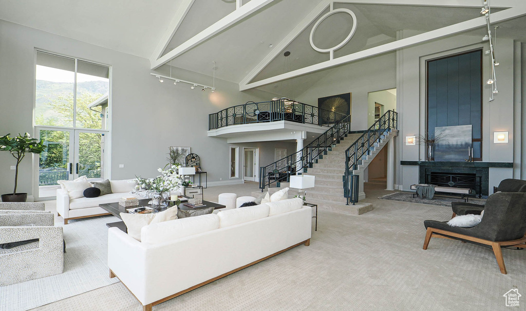 Carpeted living area featuring high vaulted ceiling, stairs, rail lighting, and beamed ceiling