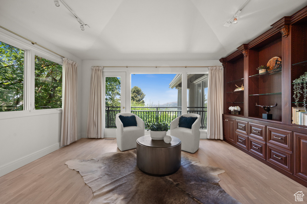 Sitting room with rail lighting, vaulted ceiling, light wood-type flooring, and healthy amount of natural light