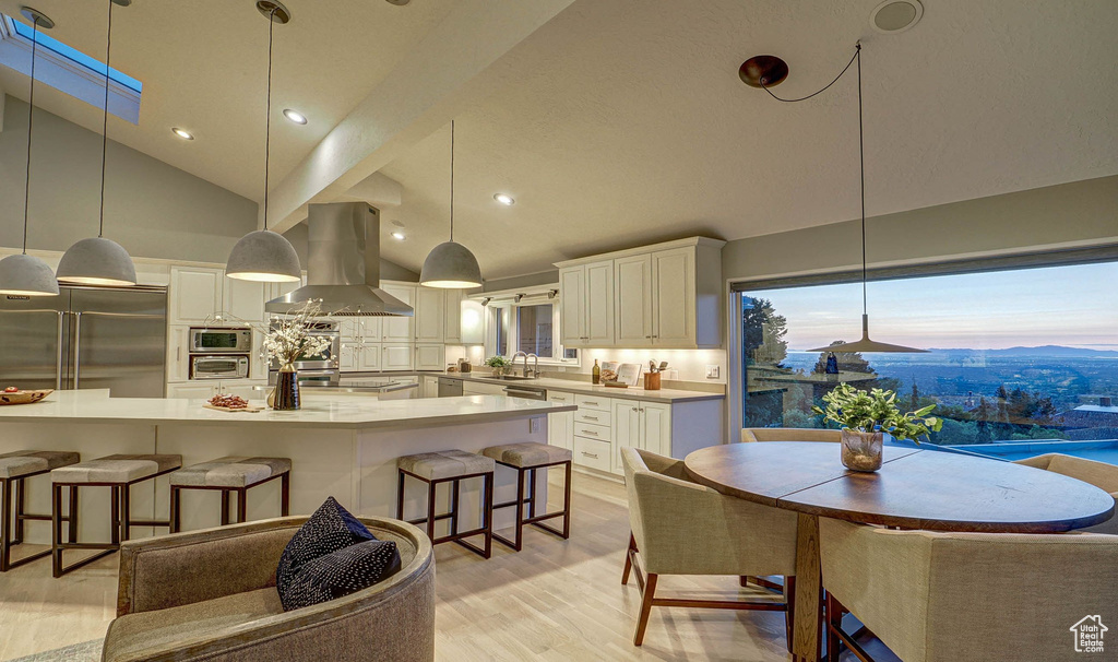Kitchen featuring island exhaust hood, appliances with stainless steel finishes, a kitchen breakfast bar, light wood-style floors, and hanging light fixtures