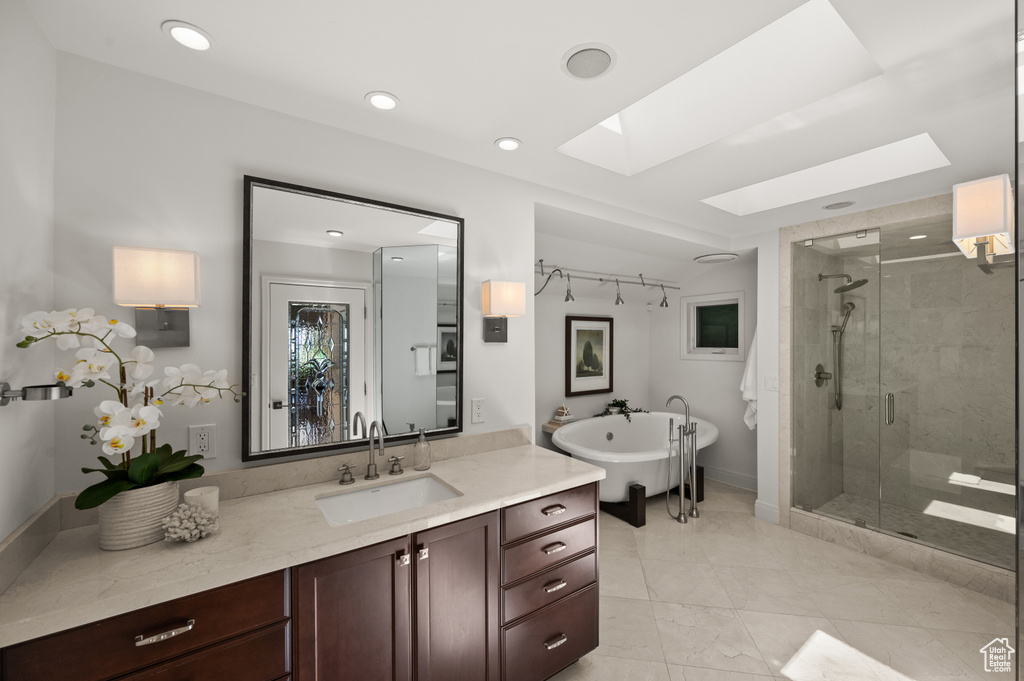 Bathroom featuring a skylight, a stall shower, vanity, a soaking tub, and recessed lighting