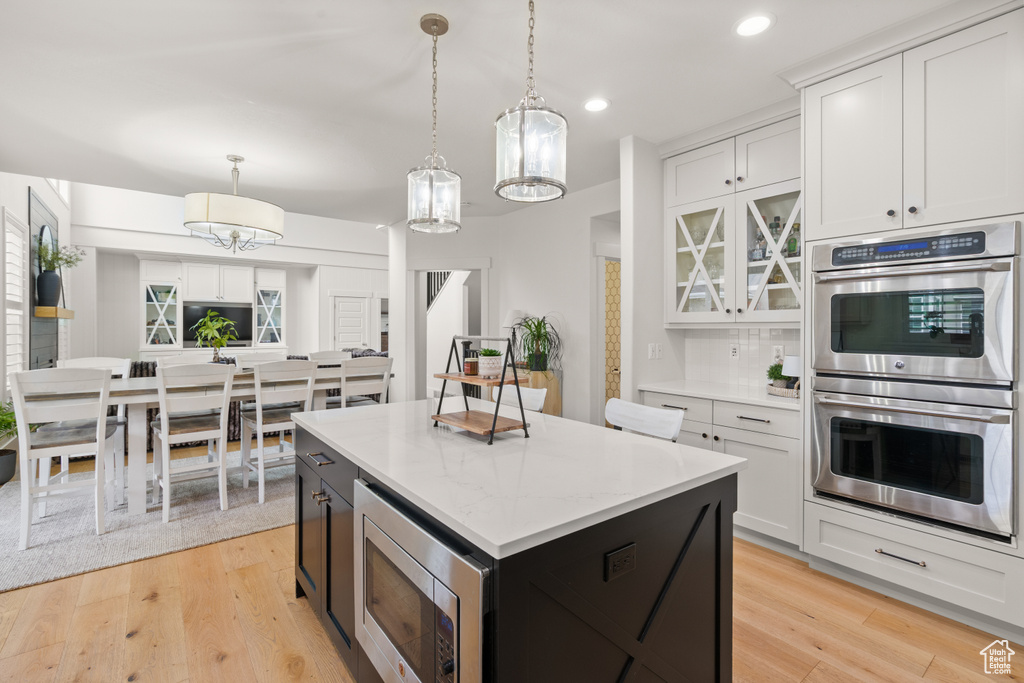 Kitchen with appliances with stainless steel finishes, decorative light fixtures, light wood finished floors, a kitchen island, and recessed lighting