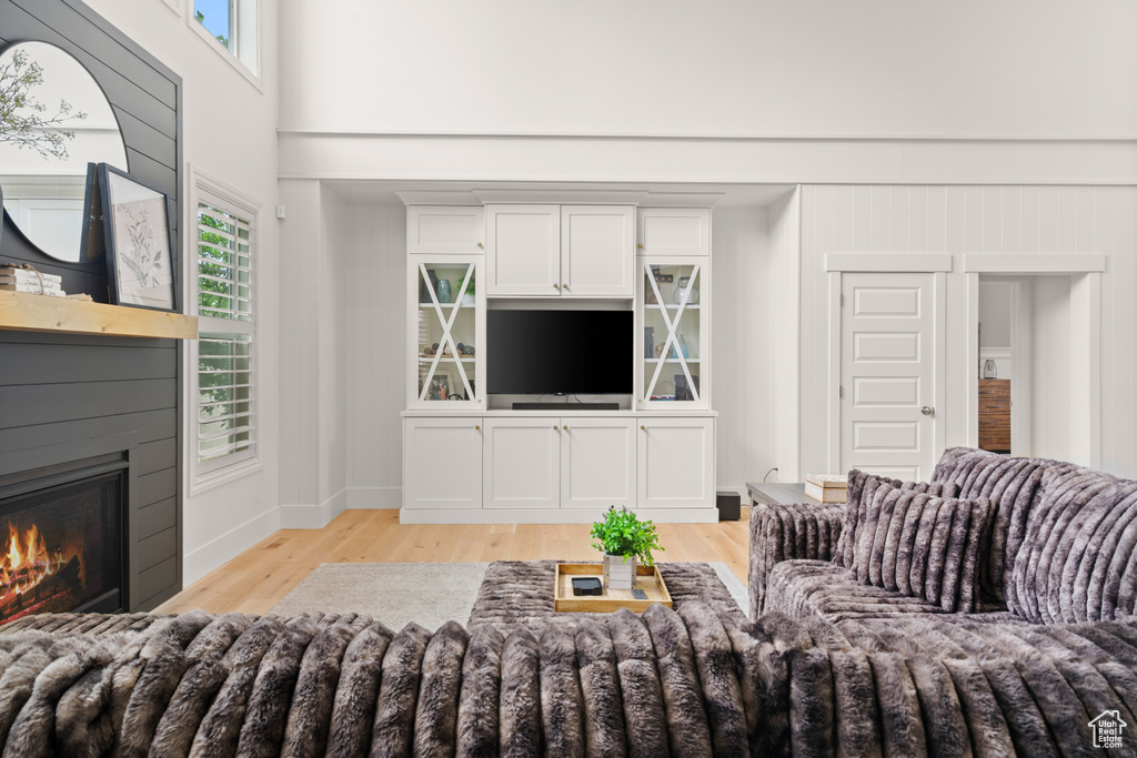 Living area featuring light wood finished floors, healthy amount of natural light, a glass covered fireplace, and a towering ceiling