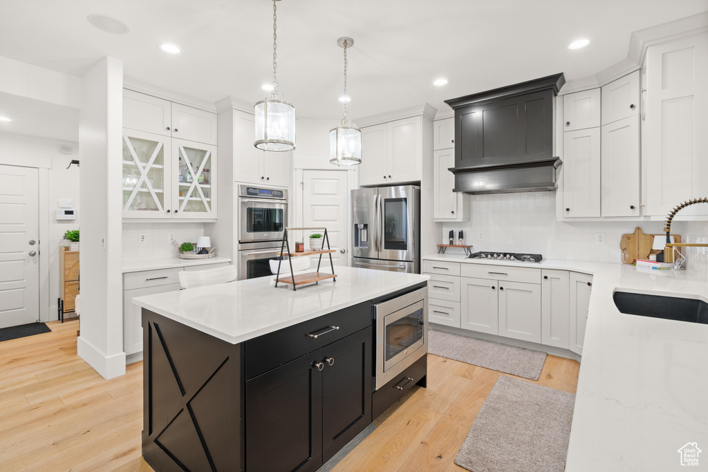 Kitchen featuring appliances with stainless steel finishes, dark cabinetry, white cabinetry, a kitchen island, and recessed lighting