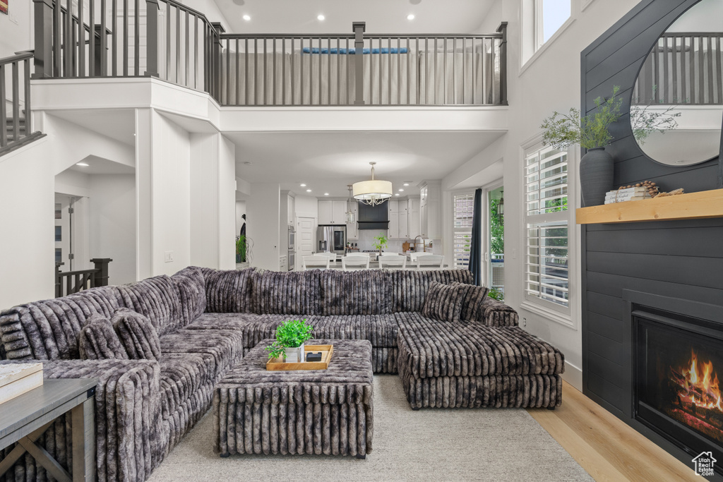 Living room featuring a high ceiling, a lit fireplace, wood finished floors, and recessed lighting