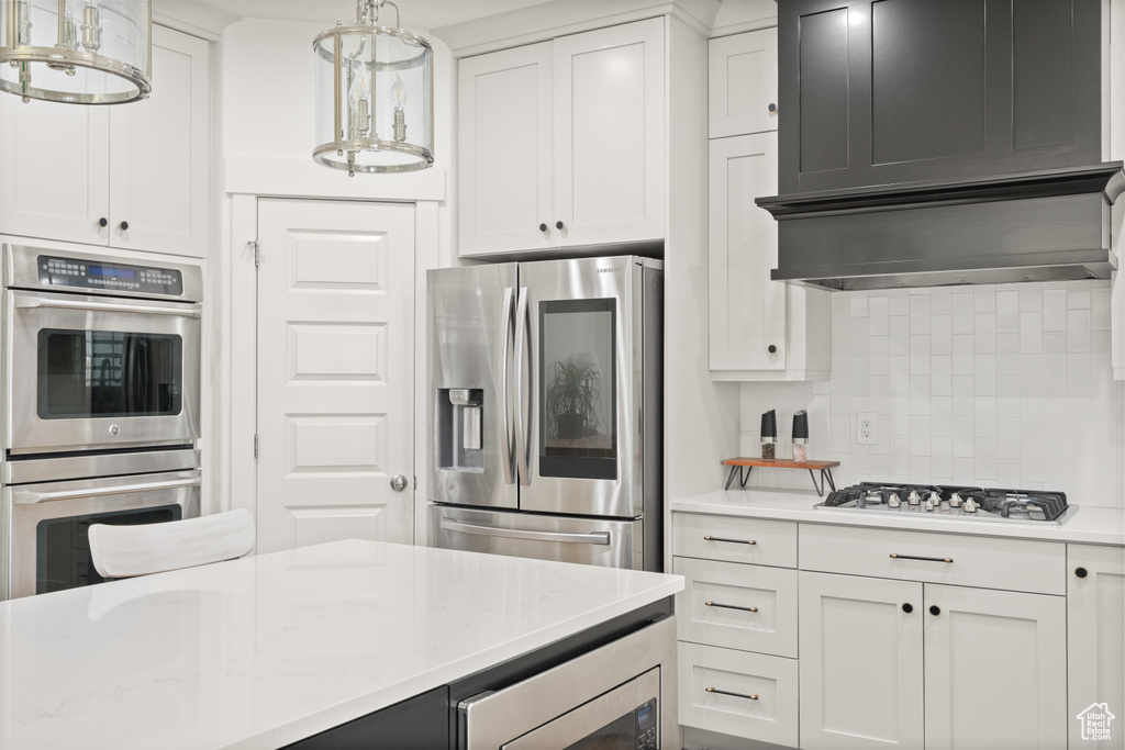 Kitchen featuring stainless steel appliances, tasteful backsplash, white cabinetry, and hanging light fixtures