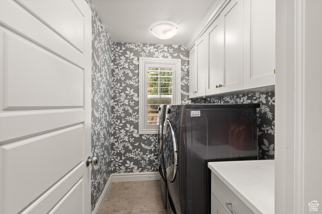 Laundry area with wallpapered walls, cabinet space, and washer / dryer