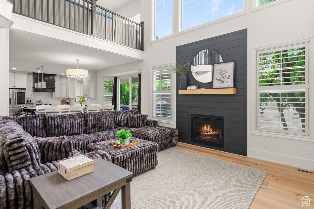 Living room featuring a high ceiling, plenty of natural light, light wood-style flooring, and a glass covered fireplace