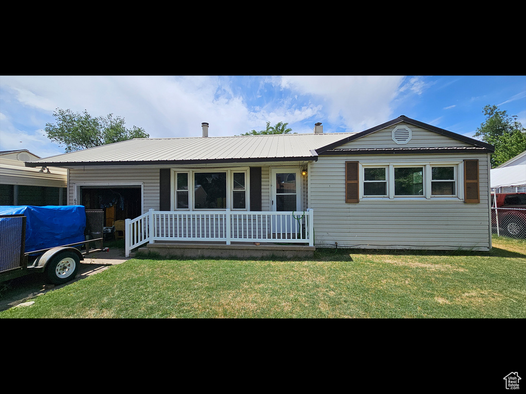 Ranch-style house featuring an attached garage, covered porch, a front yard, and a metal roof