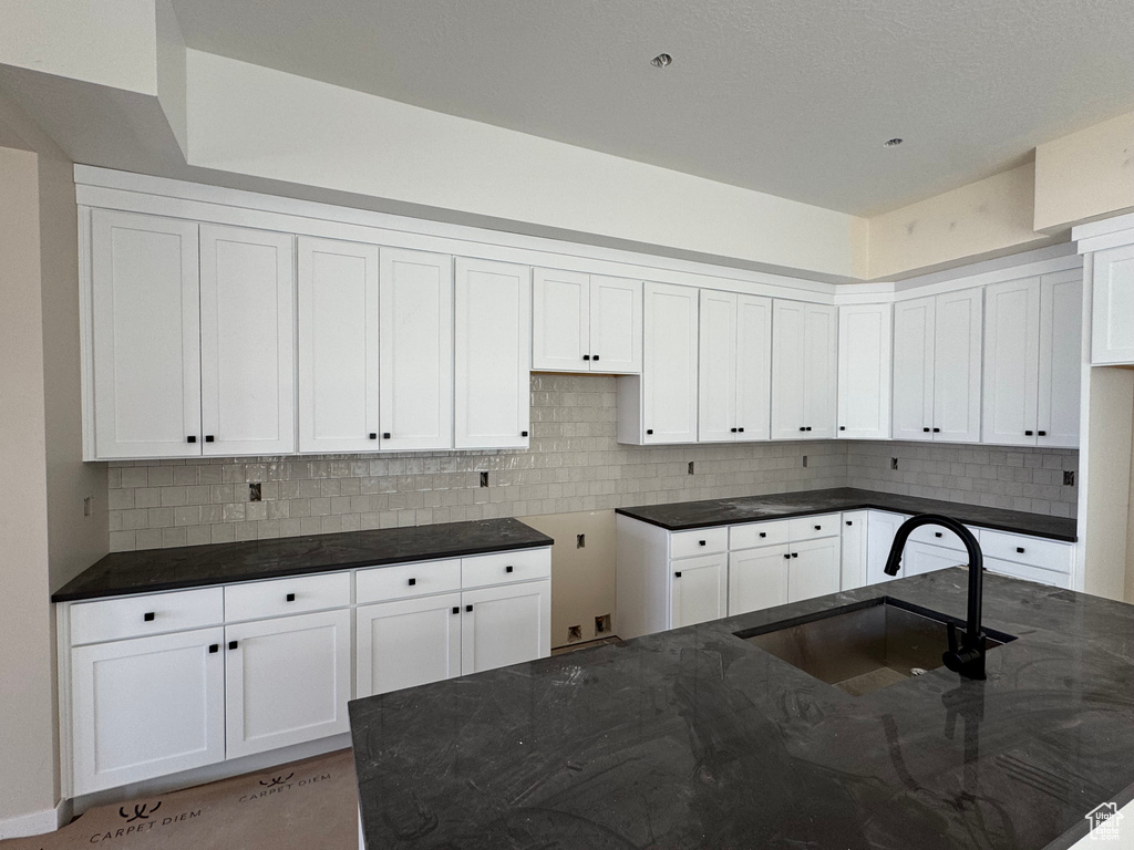 Kitchen with dark stone countertops, decorative backsplash, and white cabinets