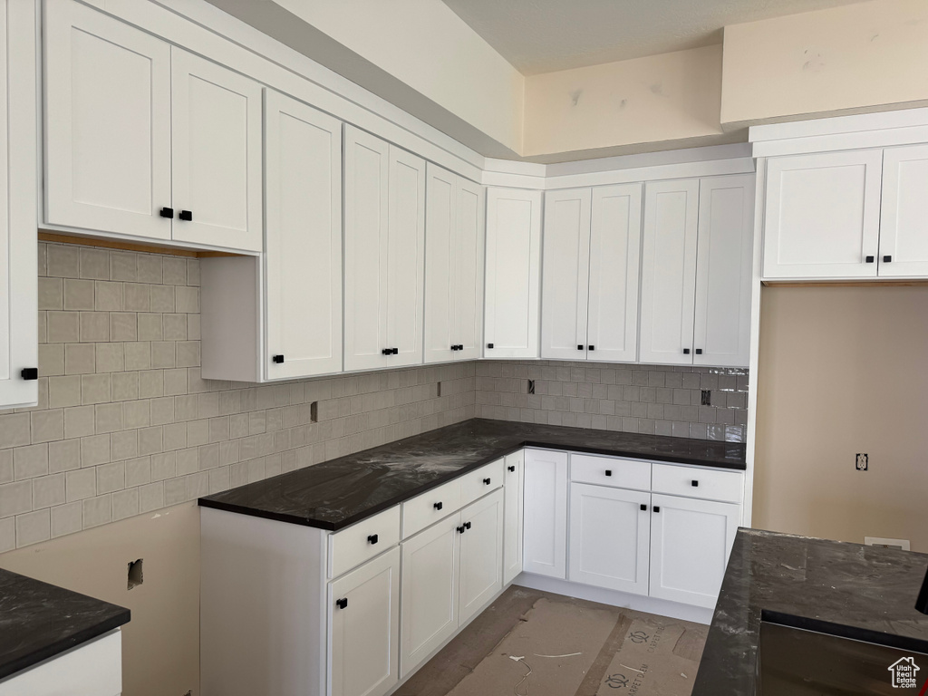 Kitchen with backsplash, white cabinets, and dark stone counters