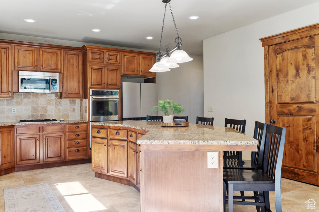 Kitchen with appliances with stainless steel finishes, a breakfast bar, recessed lighting, brown cabinetry, and pendant lighting