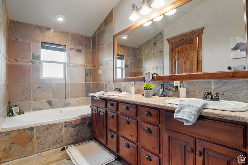 Full bathroom featuring tile walls, double vanity, vaulted ceiling, tiled tub, and tasteful backsplash