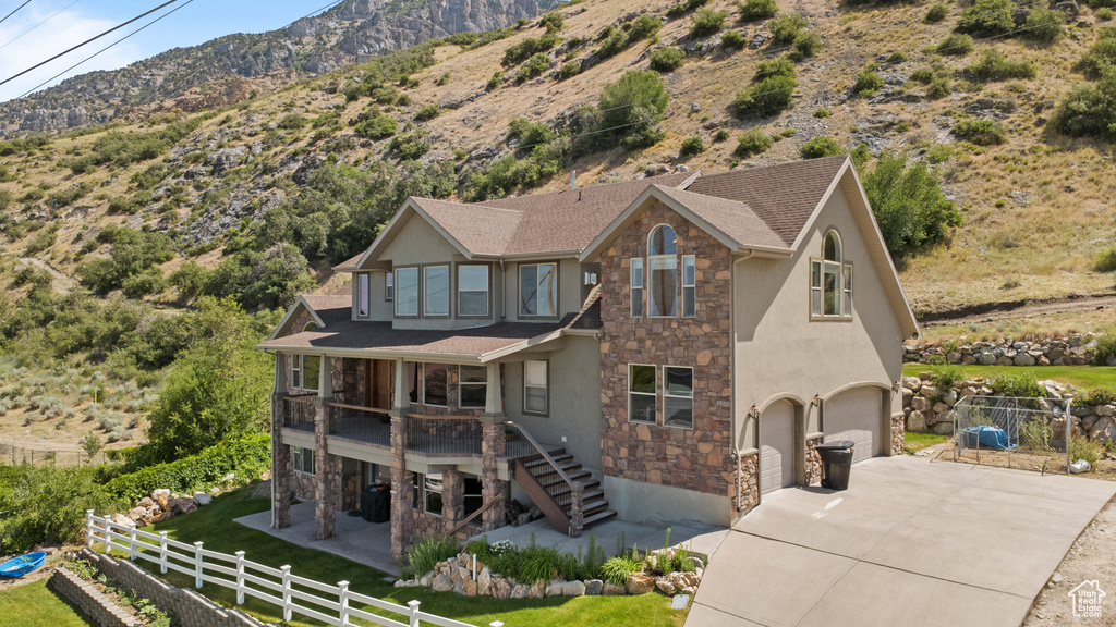 View of front facade featuring stone siding, a mountain view, concrete driveway, an attached garage, and stucco siding