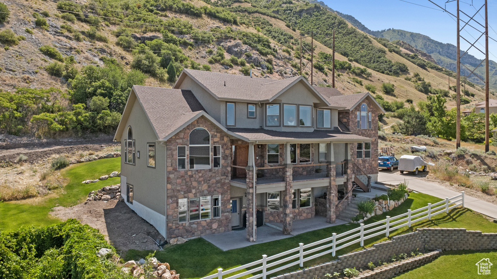 Back of property featuring stone siding, stucco siding, a patio, a mountain view, and a shingled roof
