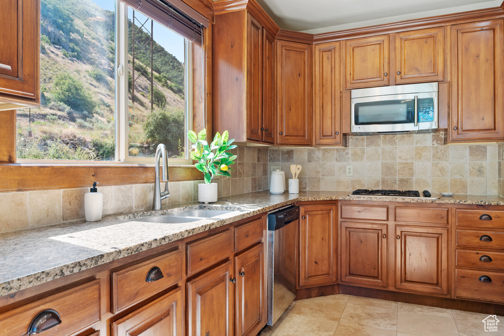 Kitchen featuring stainless steel appliances, brown cabinets, tasteful backsplash, and light stone countertops