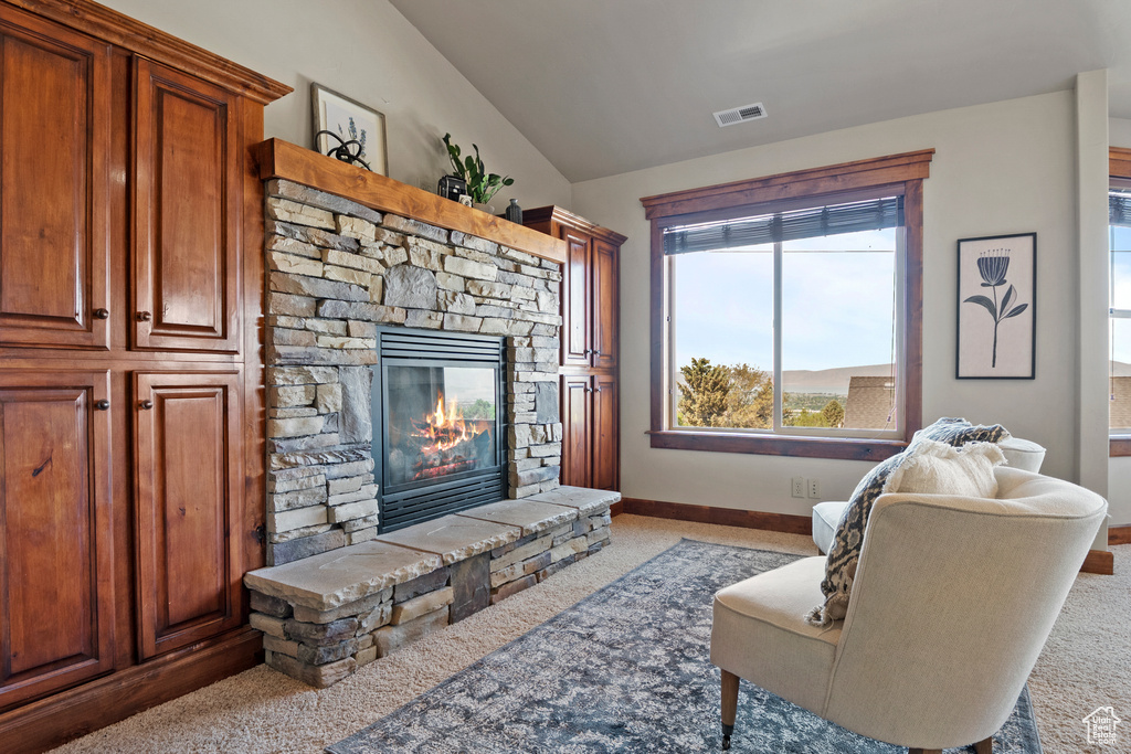 Living area with carpet flooring, a stone fireplace, and vaulted ceiling