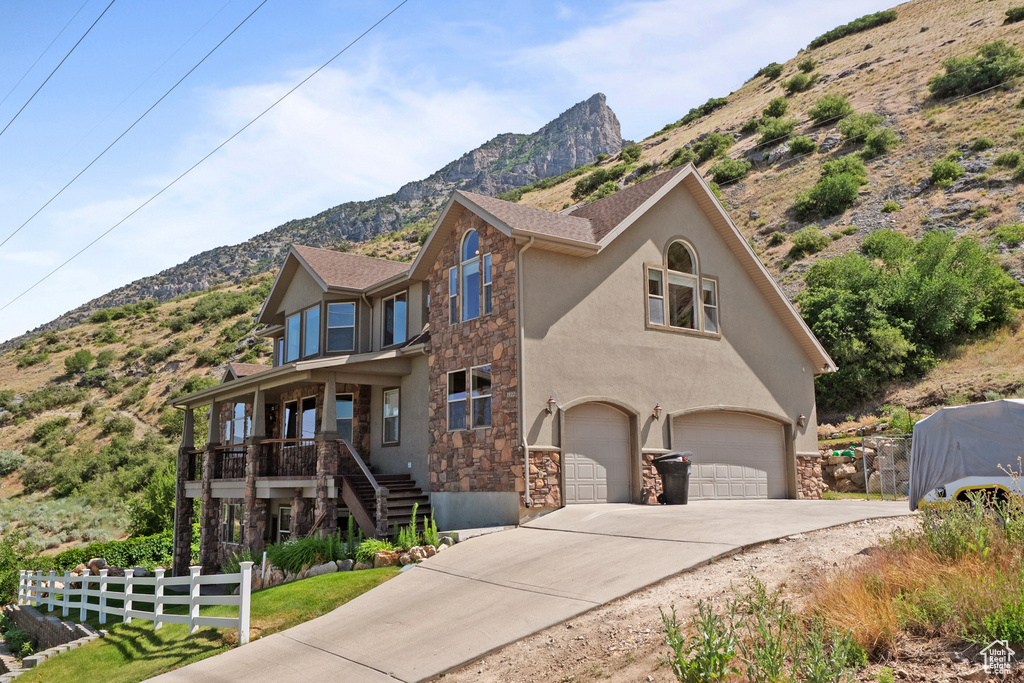 View of front of property featuring stone siding, a mountain view, a garage, concrete driveway, and stucco siding