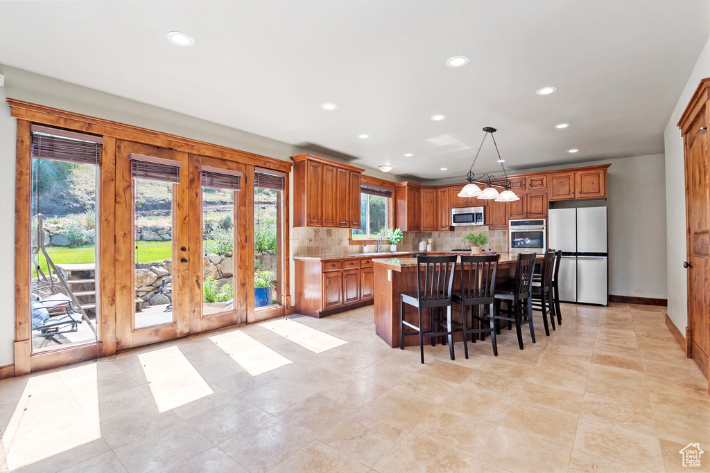 Kitchen with stainless steel appliances, recessed lighting, tasteful backsplash, a center island, and brown cabinetry