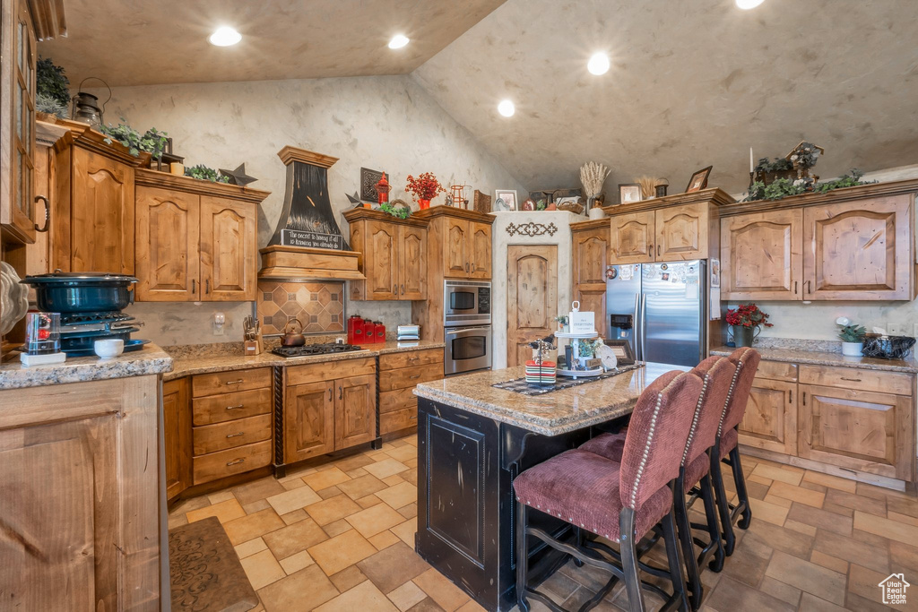 Kitchen featuring appliances with stainless steel finishes, premium range hood, light stone finish floors, high vaulted ceiling, and a center island