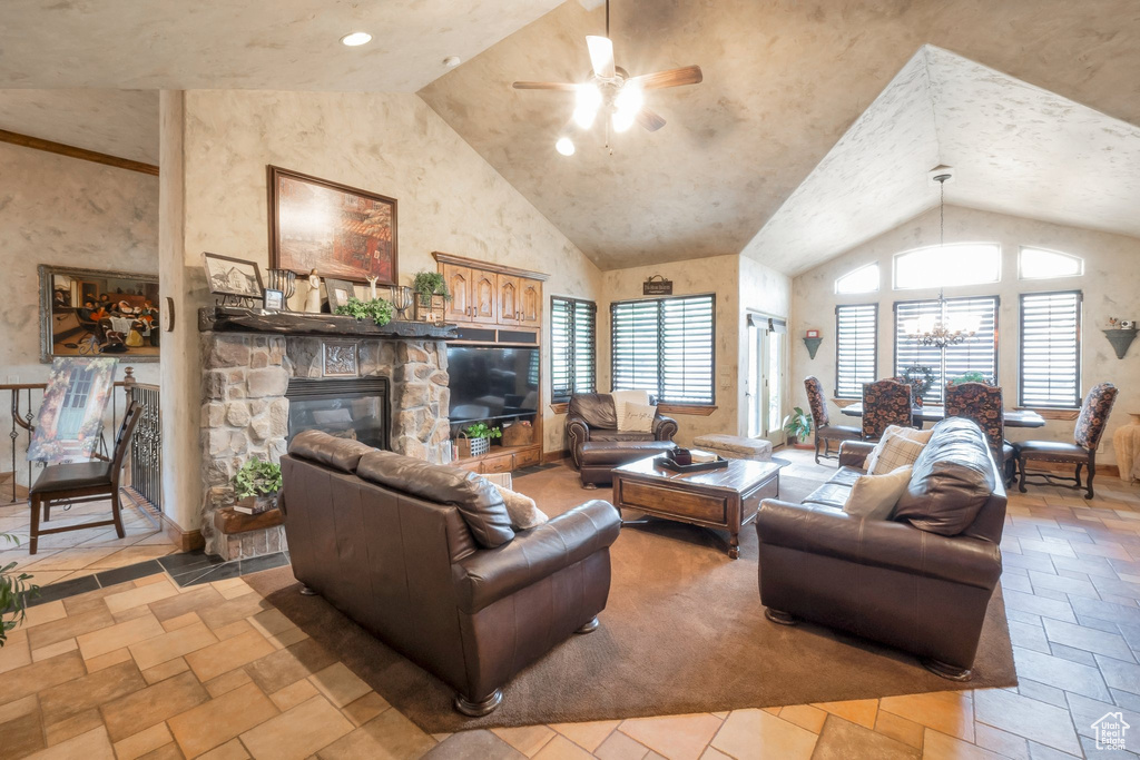 Living area featuring a ceiling fan, stone tile flooring, a stone fireplace, a chandelier, and high vaulted ceiling
