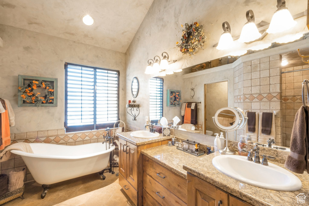 Bathroom featuring vaulted ceiling, vanity, a soaking tub, tile patterned floors, and tile walls
